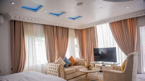 A spacious hotel room with a large bed, a sofa, a TV, and a coffee table. - MONDEESTARS LUXURY HOME (Ibadan)