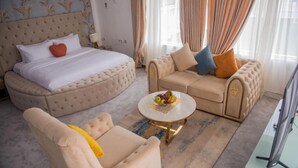 A bedroom with a large bed, a sofa, a chair, and a small round table with fruit. - MONDEESTARS LUXURY HOME (Ibadan)