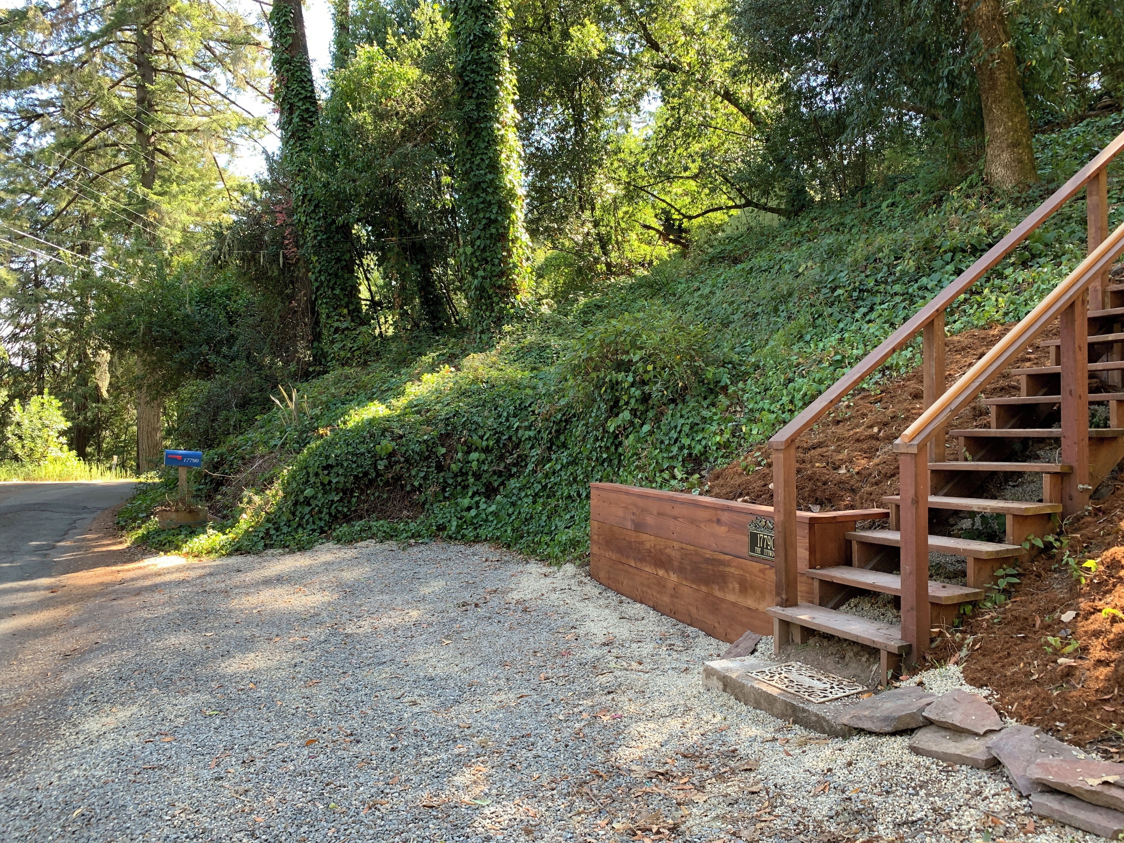 Un escalier en bois mène le long d’un chemin de gravier, bordé d’une végétation luxuriante et d’arbres.