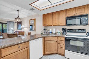 A modern kitchen with wooden cabinets, a built-in microwave, and a dishwasher. - I-451 - Spectacular Lanai Views & Sleeps 6 (Naples)