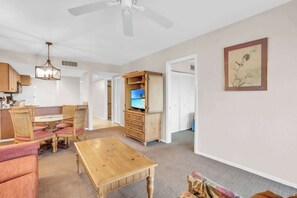 Ein geräumiges Wohnzimmer mit Couchtisch aus Holz, einem Fernseher auf einer Holzkommode und einem Deckenventilator.