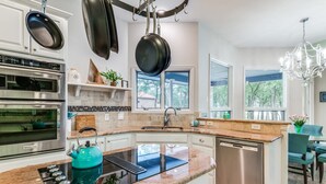 Una cocina moderna con estufa, horno y lavavajillas integrados. Hay ollas colgando y un hervidor en la pared.