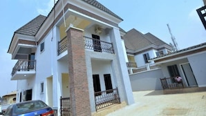 A two-story residential building with a balcony, a car parked in front, and a clear sky. - Delad Hotel and Suites (Ibadan)
