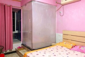 A bedroom with a wardrobe, a bed with a patterned bedspread, a window with pink curtains, and a wall-mounted air conditioner. - Jiangwen Apartment (Chongqing)