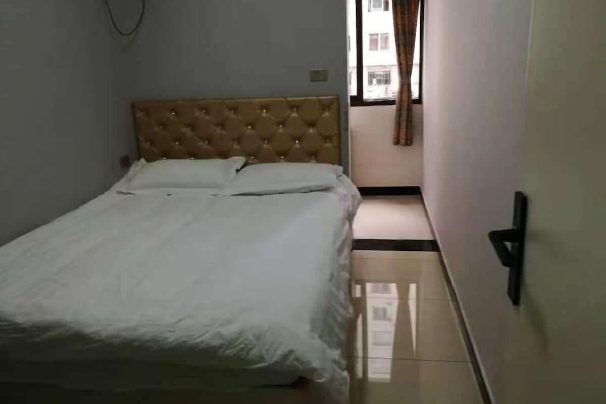 A bedroom with a tufted headboard, a bed with white linens, a small bedside table, and a window with curtains.