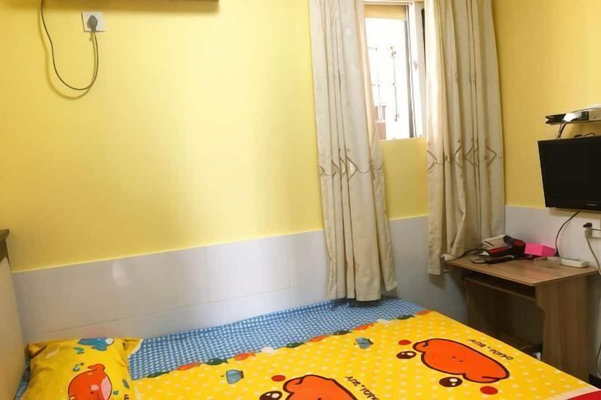 A room with a bed, a desk, a window with curtains, and a television on a stand.