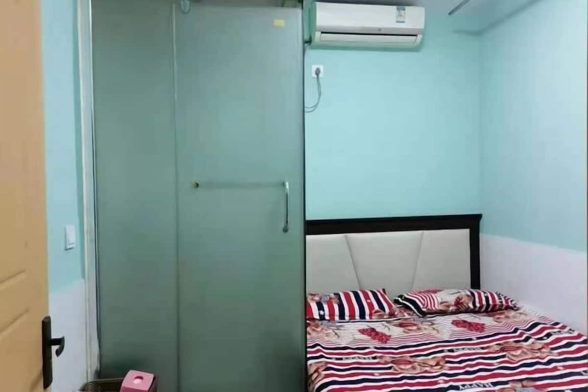 A room with a bed, a wardrobe, and an air conditioning unit.