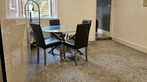 Een kleine vergaderruimte met een glazen tafel en vier stoelen, vloerbedekt met tapijt, en een raam met zonwering.