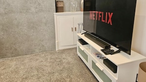 Een moderne woonkamer met een grote flatscreen televisie die aan een wit kastje is bevestigd, een afstandsbediening en een tijdschrift op het kastje.