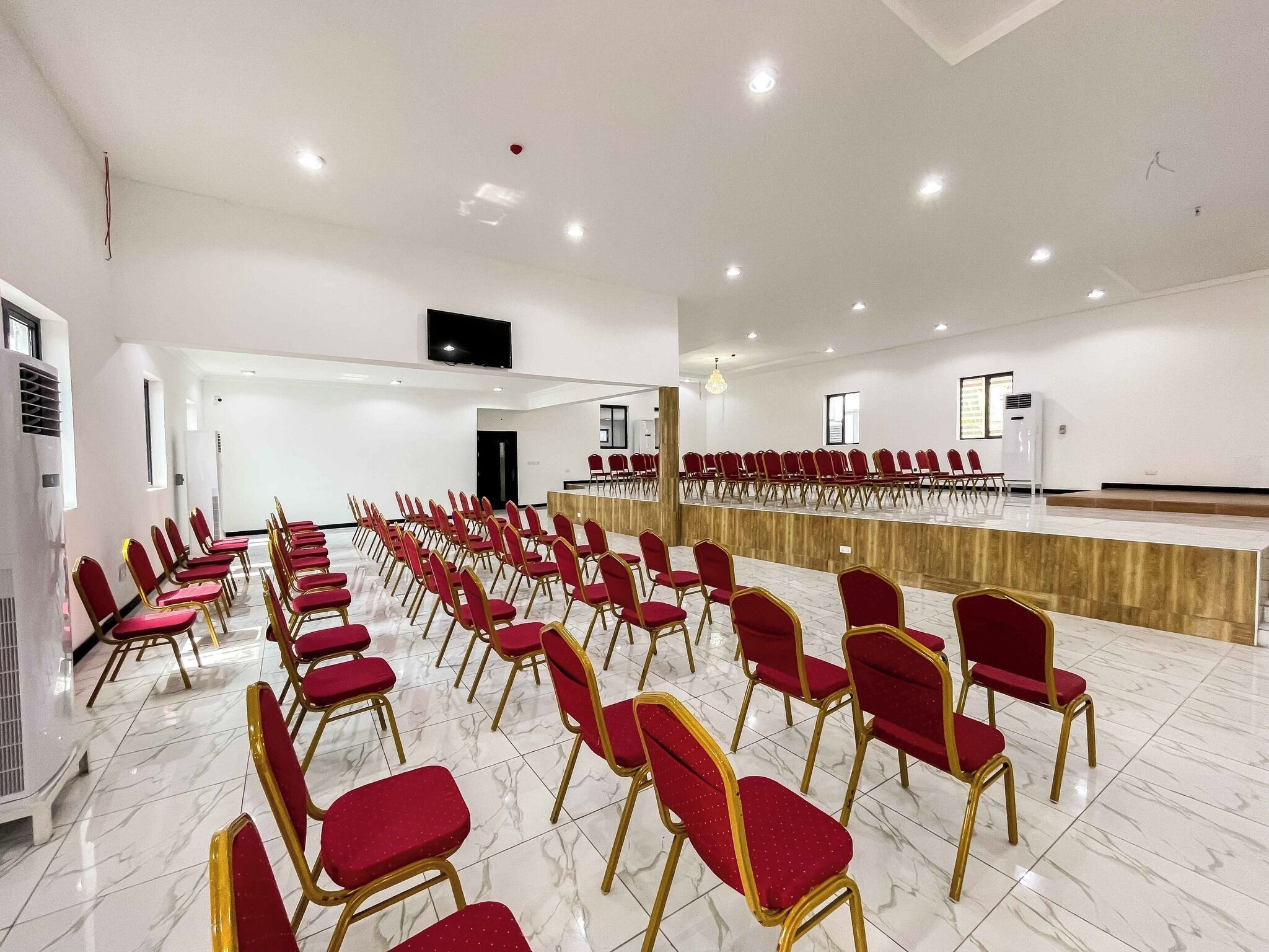 A conference room with rows of red chairs, a long table, and a large screen.