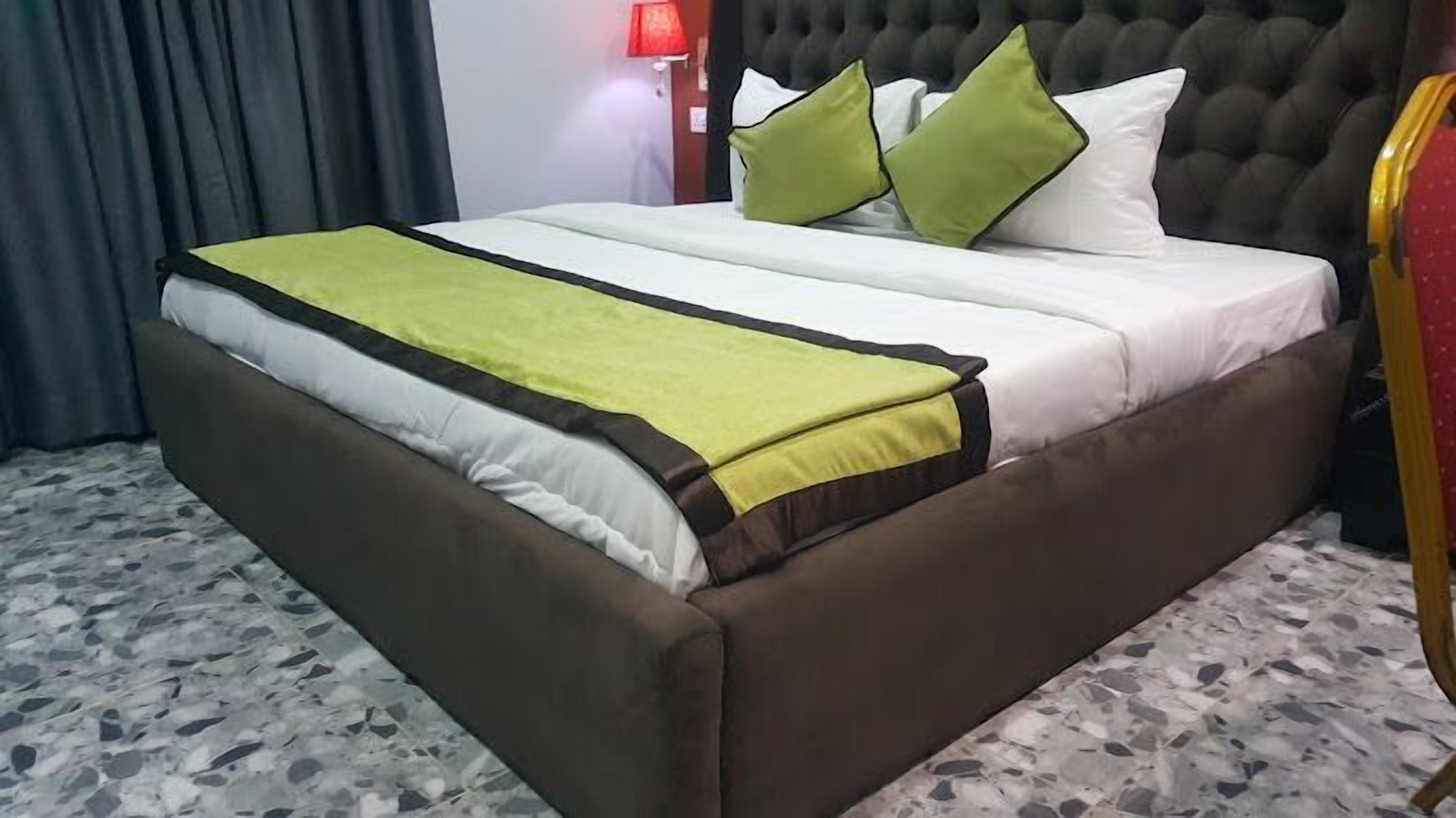 A bed with a brown frame, white bedding, and green pillows.