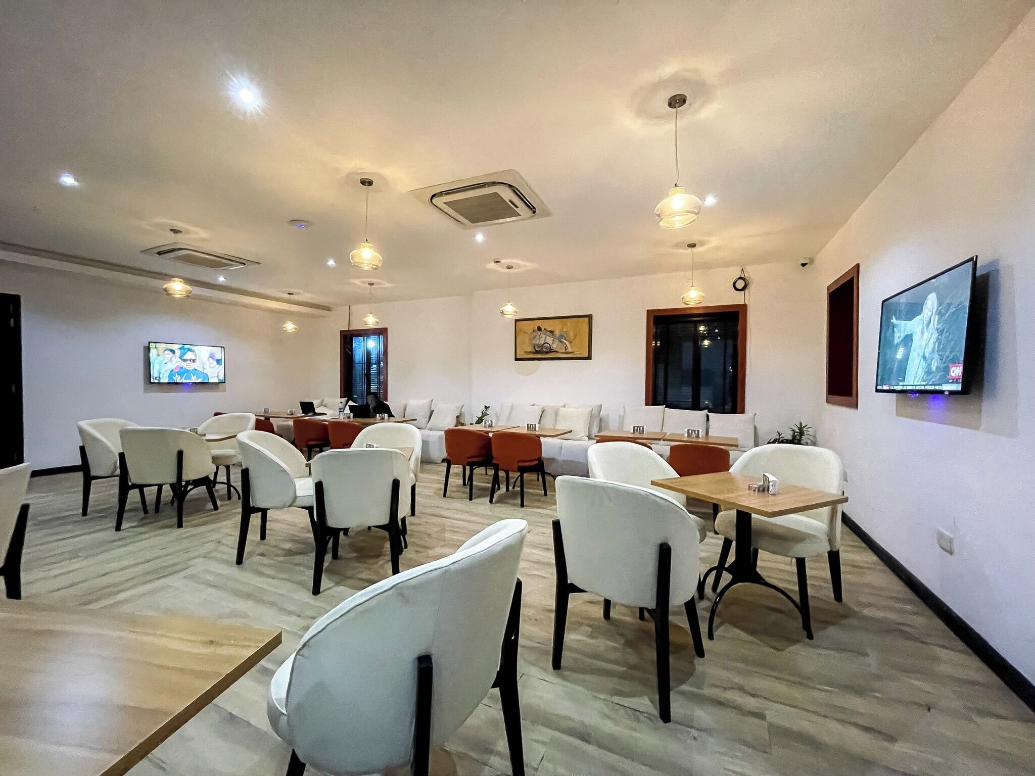 A conference room with white and orange chairs, a TV on the wall, and a ceiling with recessed lighting.
