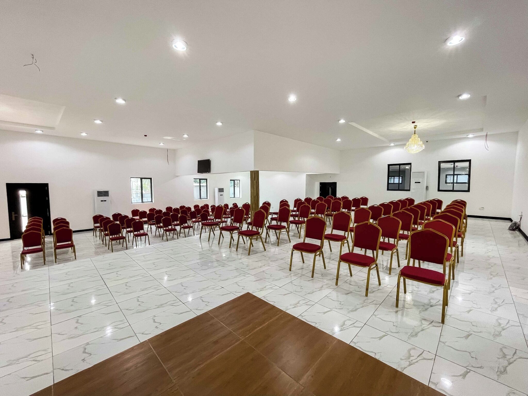 Una grande sala conferenze con file di sedie rosse, pareti bianche e pavimento in marmo.