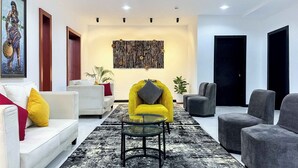 A modern living room with a white sofa, a yellow armchair, and grey armchairs. There is a black and white patterned rug on the floor. - The Citron Hotels (Ibadan)