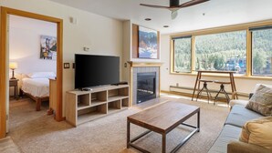 Un salón con chimenea, televisor y un ventanal con vistas a árboles y edificios.