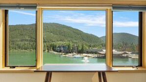 Una habitación con un ventanal que da a un lago y colinas boscosas.