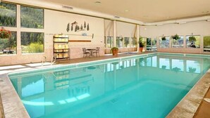 Una piscina interior con paredes de vidrio transparente, una zona de bar y un área de estar con vistas al exterior.
