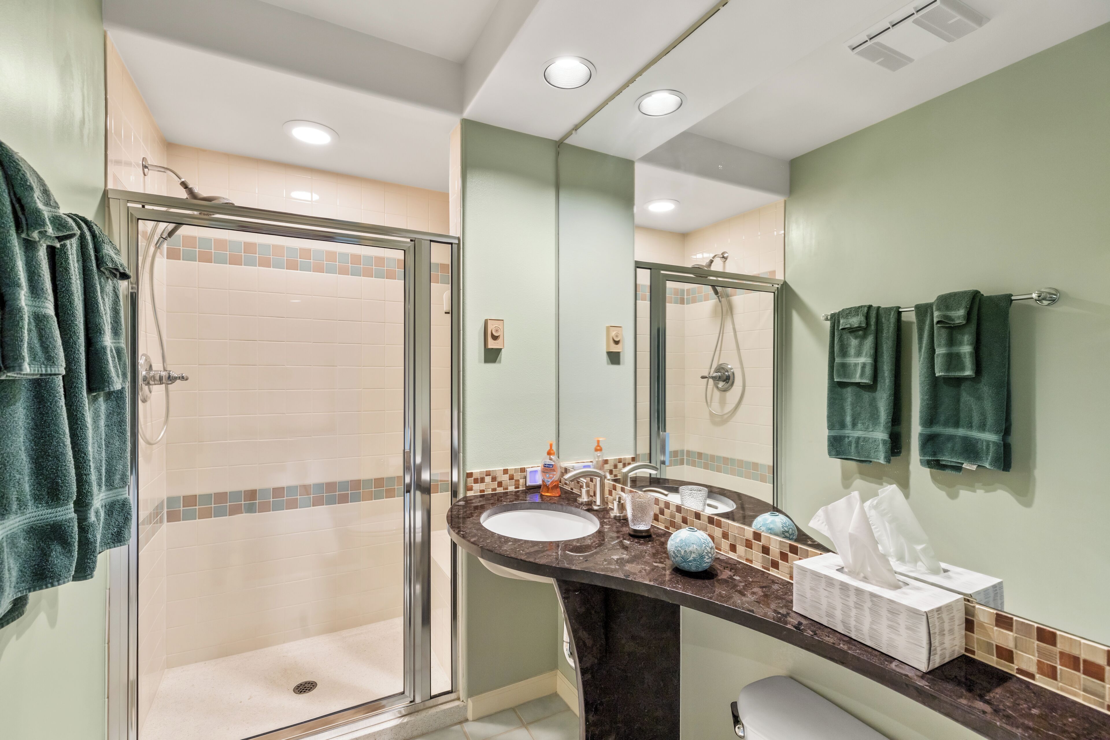 Une salle de bain dotée d’une douche à parois de verre, d’un lavabo avec un plan de travail en marbre et d’un miroir auquel sont accrochées deux serviettes.