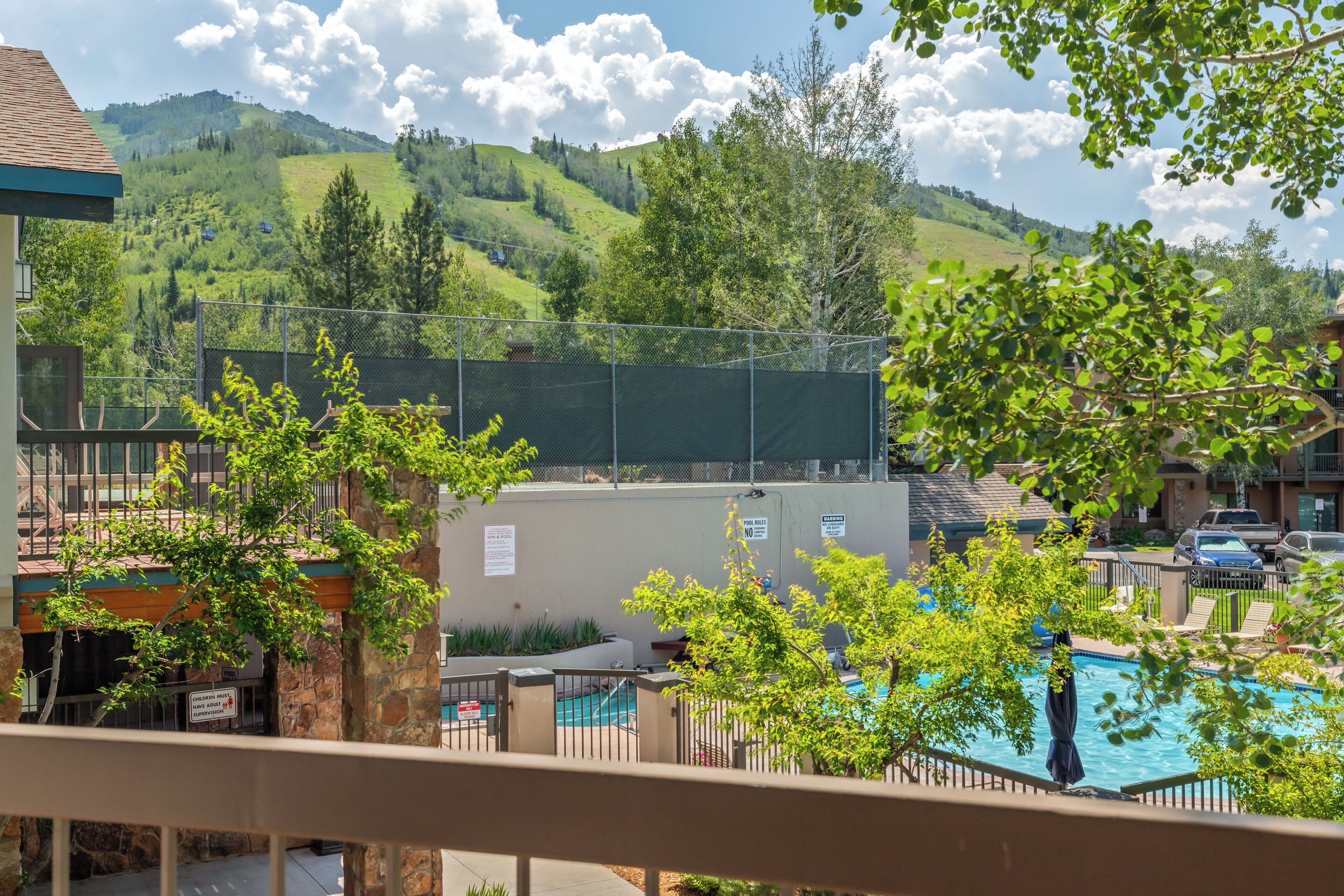 A pool area with a view of a mountain, surrounded by trees and a fence.