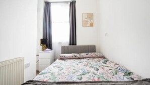 A bedroom with a bed, a nightstand, a radiator, a window with curtains, and a wall art piece. - Charming London Apartment Near Hyde Park (London)