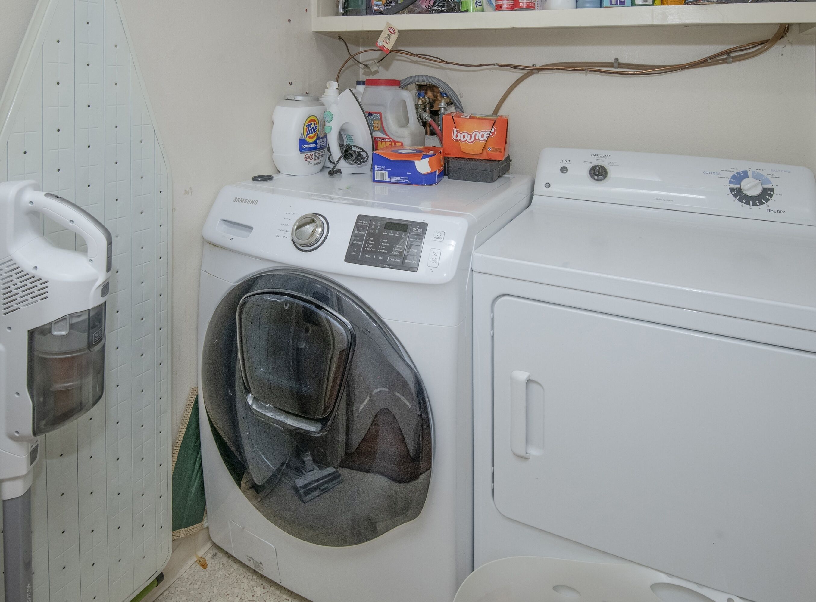 Un área de lavandería con lavadora de carga frontal, secadora y un estante superior con productos de limpieza.