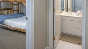 Una habitación con literas y un baño que incluye un lavamanos y un espejo.