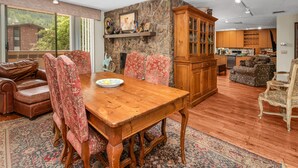 Un salón espacioso con una mesa de comedor de madera, sillas tapizadas con motivos florales, una pared de acento de piedra y vistas a un edificio de ladrillo.