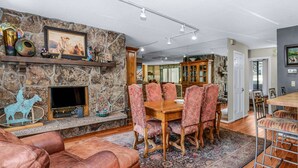 Una sala de estar con chimenea de piedra, sofá de cuero, mesa de comedor con sillas y alfombra estampada.