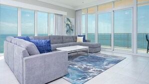 Una sala de estar moderna con un sofá seccional gris, una mesa de centro y un gran ventanal con vista al mar.