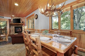 A rustic dining area with a wooden table set for four, a stone fireplace, and large windows offering a view of the outdoors. - Timber Wolf Lodge 10d 2 Bedroom Condo by RedAwning (Park City)