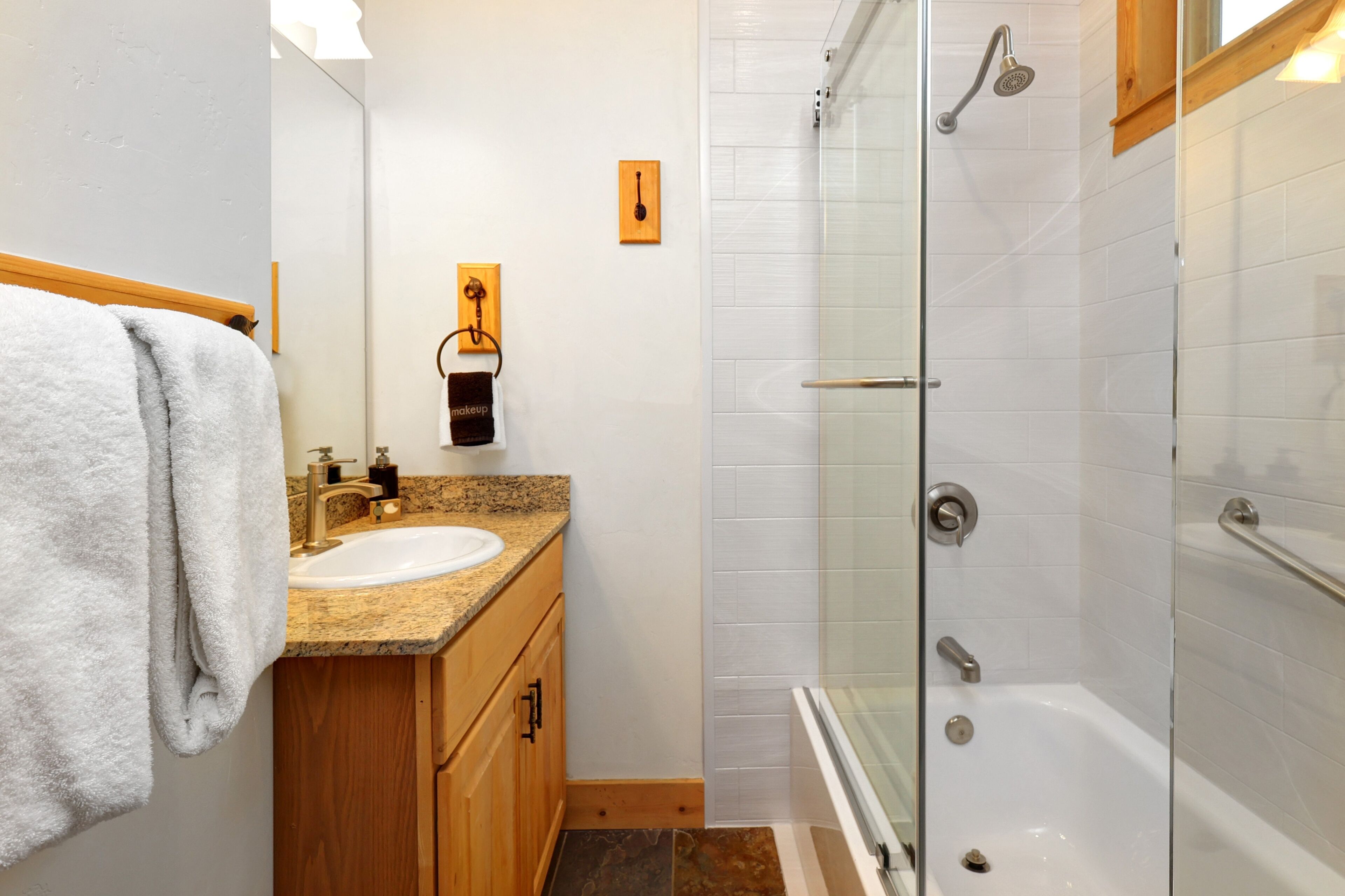 A bathroom with a granite countertop sink, wooden cabinets, a glass shower enclosure, and a white tiled shower area.