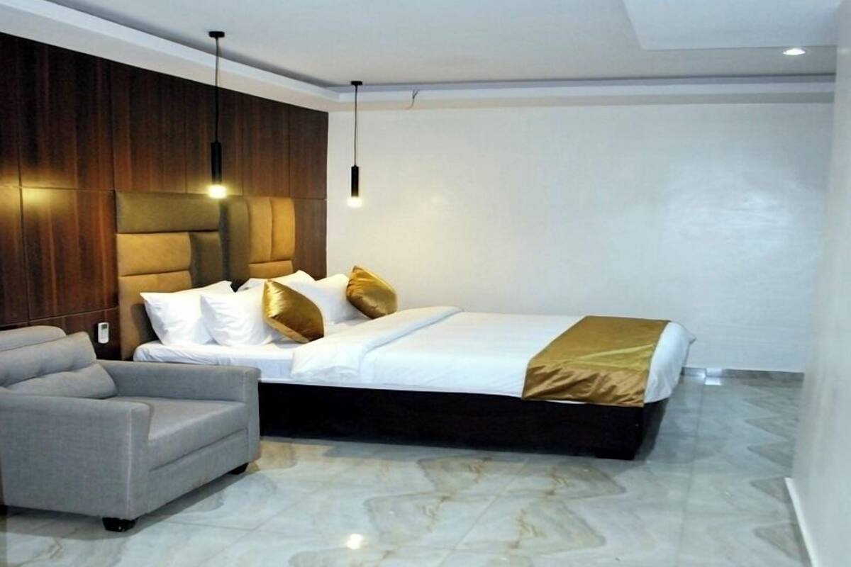 A modern hotel room with a large bed, a sofa, a wooden accent wall, and a marble floor.