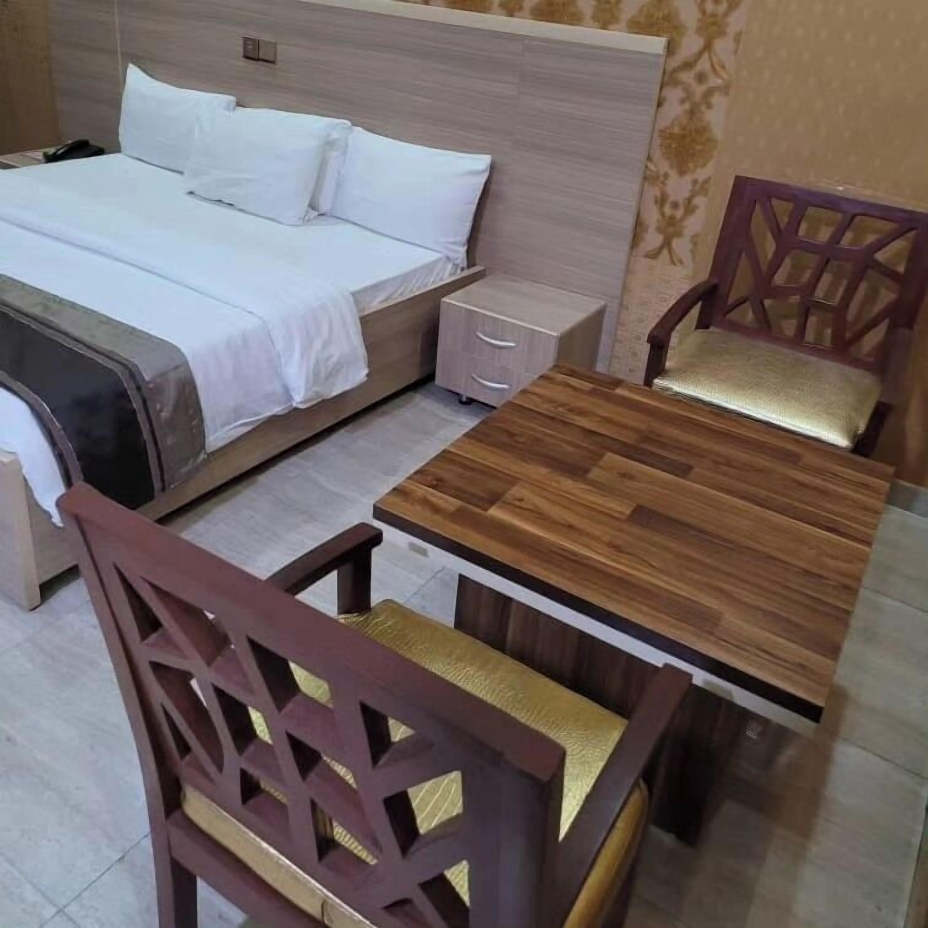 A hotel room with a bed, bedside table, nightstand, and a wooden dining table with two chairs.