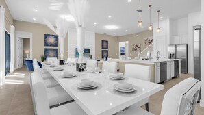 Un espace repas moderne avec une longue table blanche dressée pour six personnes, entourée de chaises blanches.