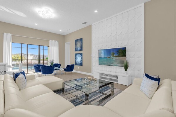 A spacious living room with a large TV, comfortable seating, and a view of the outdoors.
