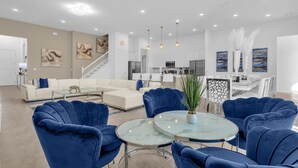 Un vaste espace de vie avec une cuisine moderne en arrière-plan, un coin repas avec une table et des chaises blanches, et un escalier menant à un autre niveau.