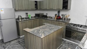 A kitchen with a central island, a refrigerator, a microwave, a stove, and various kitchen utensils. - Ashokas Hotel Ibadan (Ibadan)