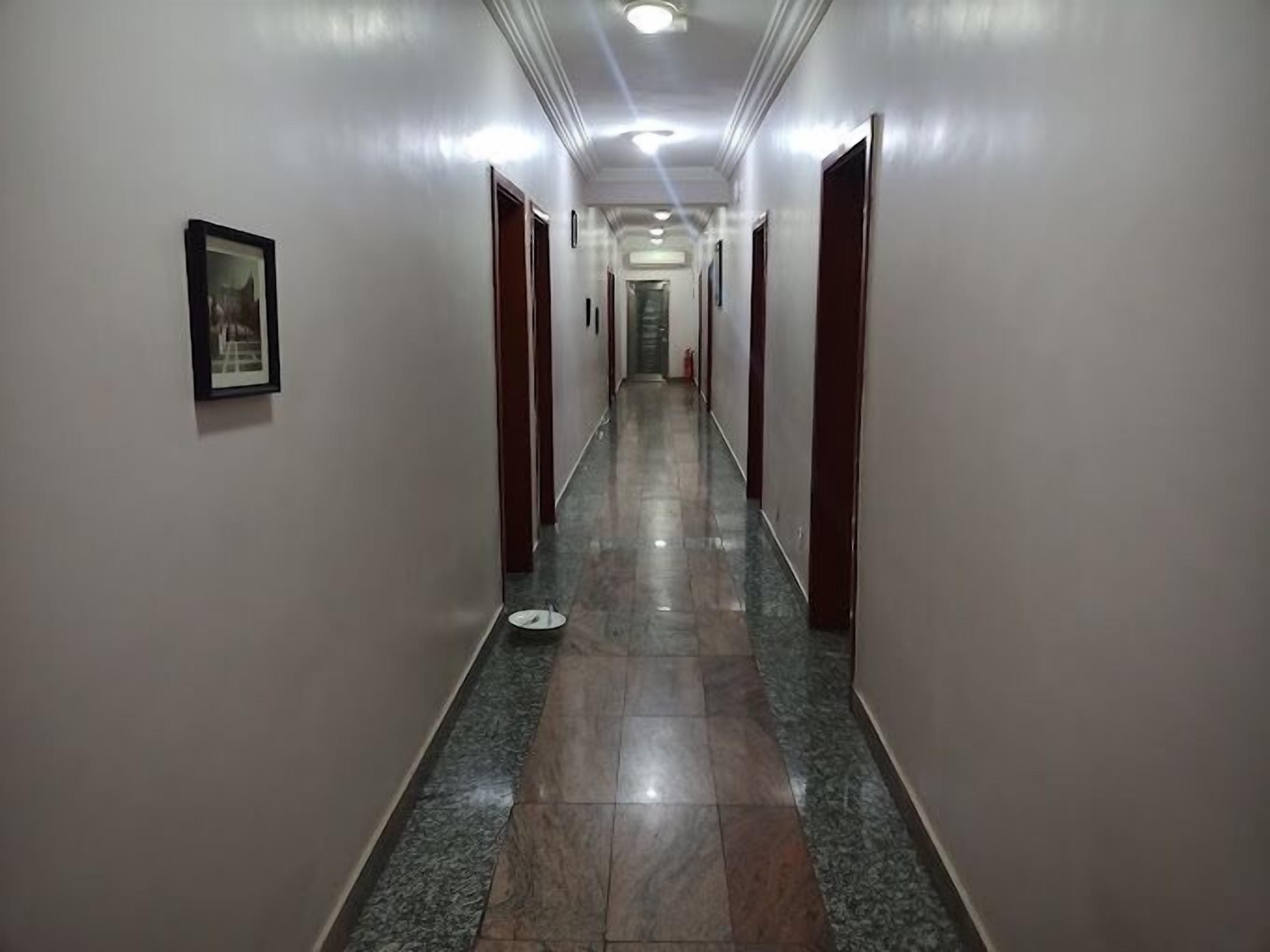 A long, narrow hallway with marble flooring and doors on both sides.