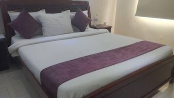 A standard hotel room with a wooden bed frame, white bedding, and a purple throw blanket.