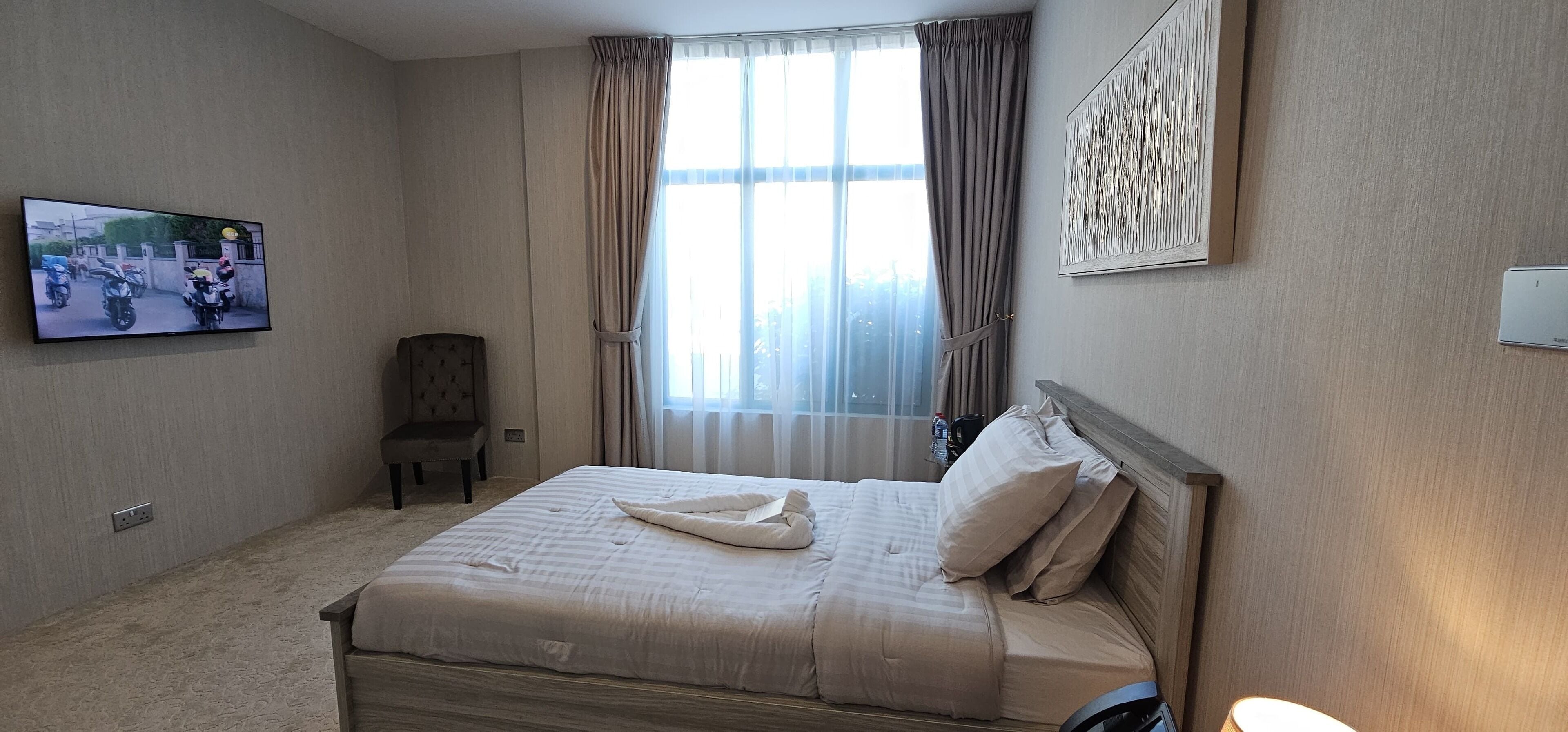 A hotel room with a bed, a chair, a television, and a window with curtains.