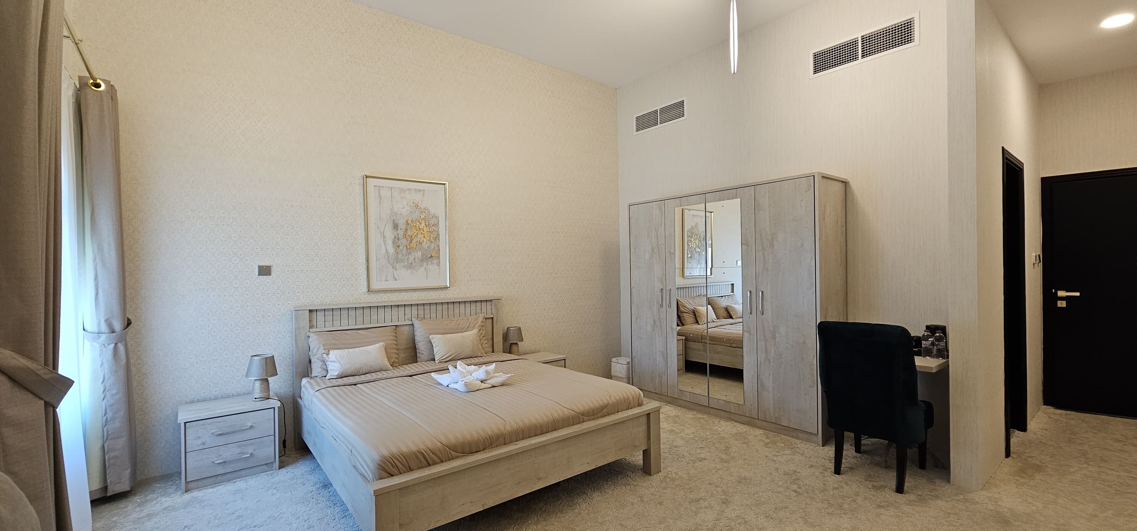 A bedroom with a bed, nightstand, wardrobe, and a desk with a chair.