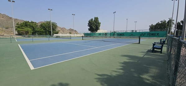 A tennis court with a net, surrounded by a chain-link fence, and branded with "YOMEX."