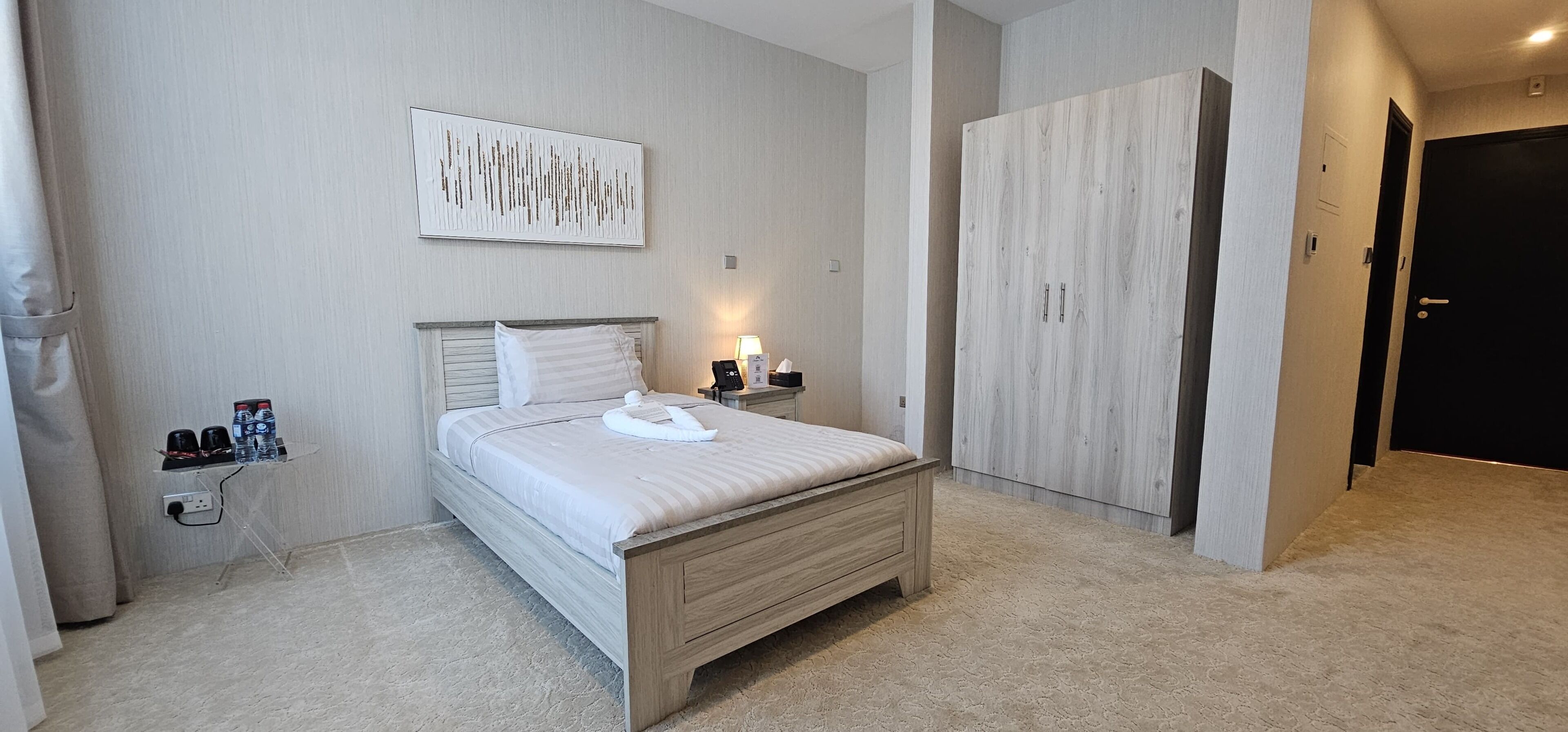 Un dormitorio ordenado con cama, mesitas de noche, armario y una obra de arte en la pared.
