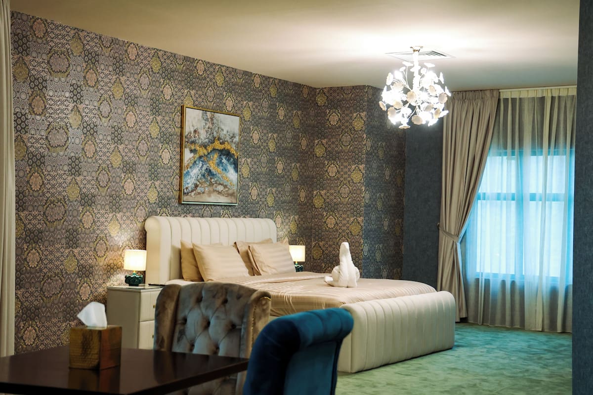 Ein Hotelzimmer mit Bett, einer Chandelüster, einem Gemälde und Blick ins Freie.