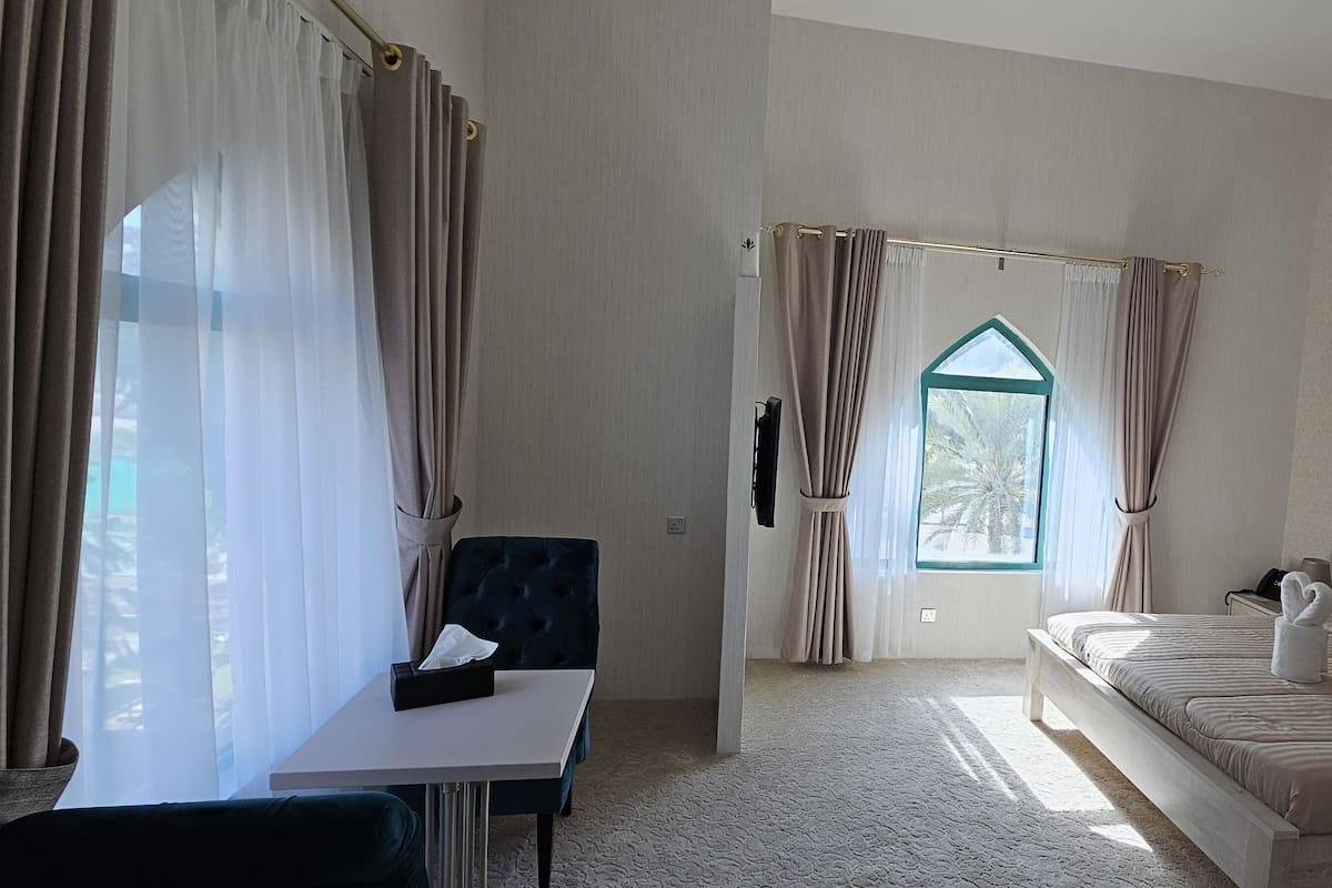 Ein Hotelzimmer mit Bett, Schreibtisch, Stuhl, einem Fenster mit Vorhängen und einem Wandbild.