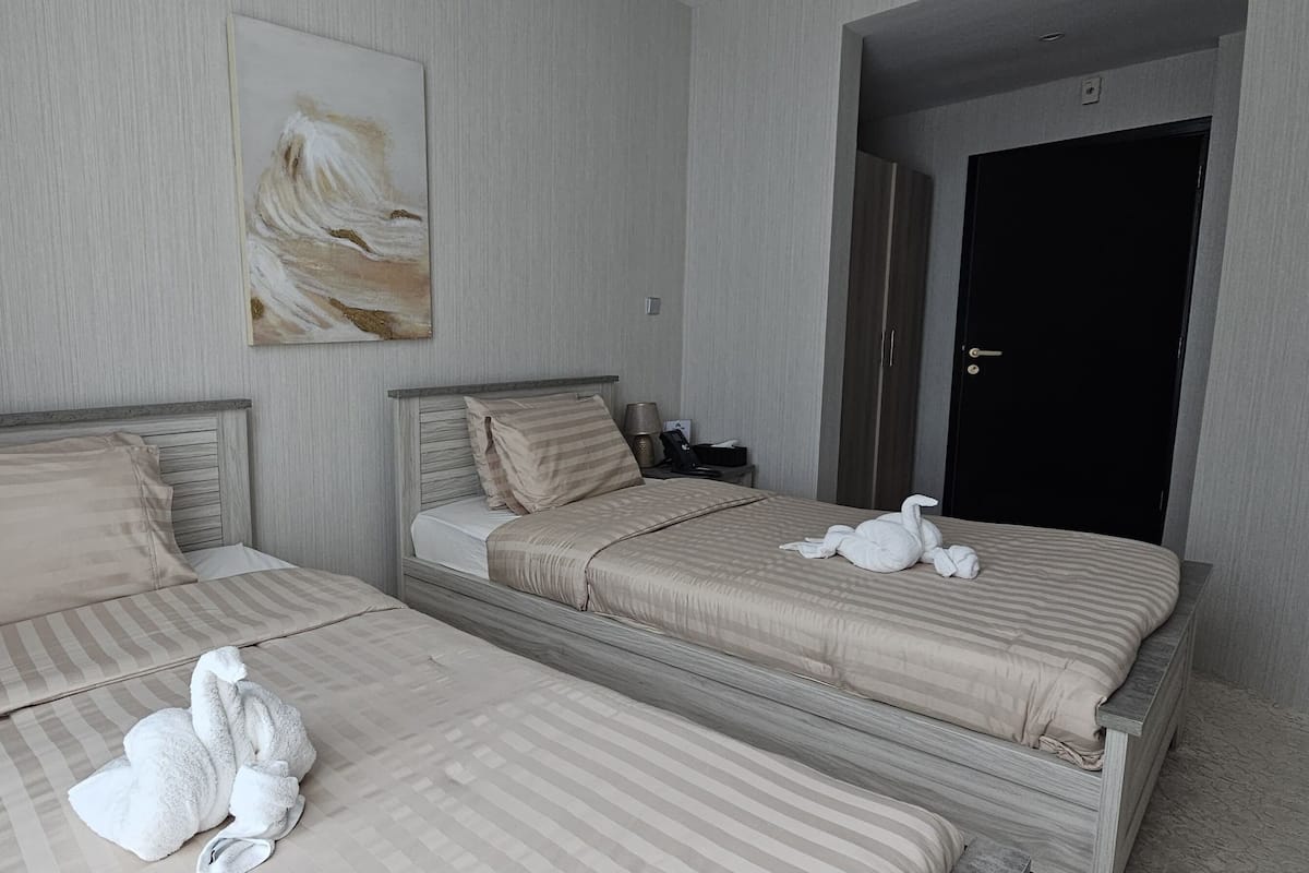 Ein Hotelzimmer mit zwei Betten, beide mit gestreifter Bettwäsche und Kissen. Über den Betten hängt ein Gemälde und rechts ist eine Tür zu sehen.