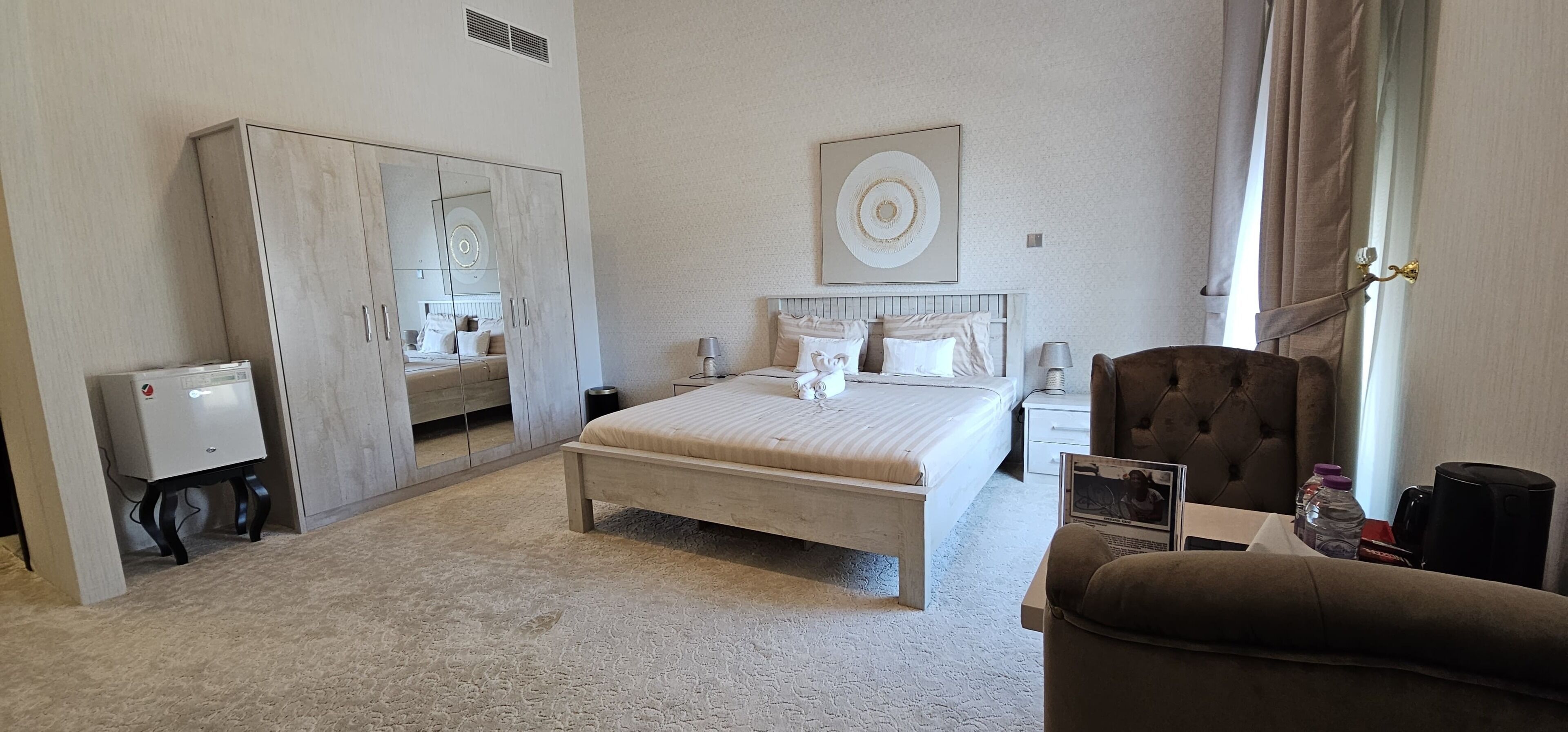 Una habitación de hotel con cama, armario, mesita de noche, silla y un espejo grande.
