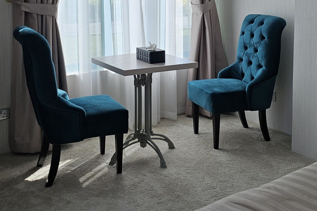 Una habitación de hotel con dos sillones azules, una mesita y una cama.