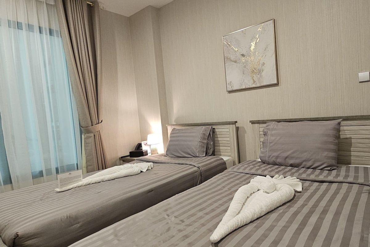 Ein Hotelzimmer mit zwei Betten, einem Nachttisch, einer Lampe und einem Fenster mit Vorhängen.