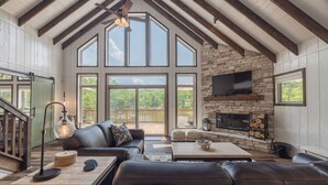 A spacious living area with a stone fireplace, leather furniture, and large windows offering a view of the outdoors.